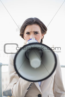 Frowning stylish brown haired businesswoman speaking in a megaphone