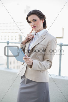 Thinking stylish brown haired businesswoman holding a tablet pc
