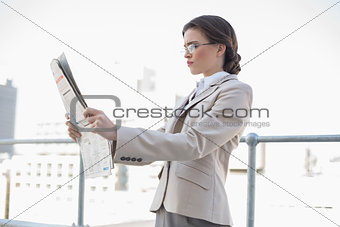 Serious stylish brown haired businesswoman reading a newspaper