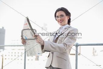 Cheerful stylish brown haired businesswoman reading a newspaper