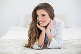 Pensive casual brown haired woman in white pajamas lying on her bed