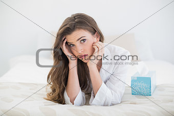 Depressed casual brown haired woman in white pajamas lying on her bed