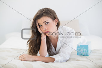 Worried casual brown haired woman in white pajamas lying on her bed