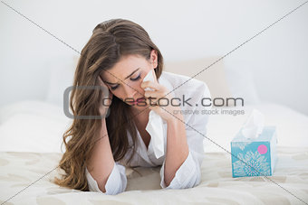 Depressed casual brown haired woman in white pajamas crying on her bed