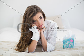 Sad casual brown haired woman in white pajamas crying on her bed