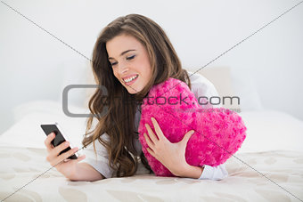 Content casual brown haired woman in white pajamas using her mobile phone