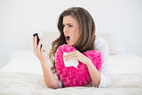 Angry casual brown haired woman in white pajamas hanging up her mobile phone