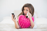 Depressed casual brown haired woman in white pajamas hanging up her mobile phone