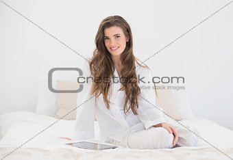Cheerful casual brown haired woman in white pajamas sitting on her bed