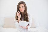 Amused casual brown haired woman in white pajamas eating popcorn