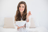Delighted casual brown haired woman in white pajamas eating popcorn