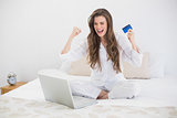 Successful casual brown haired woman in white pajamas shopping online with her laptop