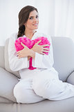 Peaceful casual brown haired woman in white pajamas hugging a heart shaped pillow