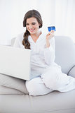 Laughing casual brown haired woman in white pajamas shopping online with her laptop