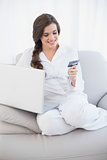 Attractive casual brown haired woman in white pajamas shopping online with her laptop