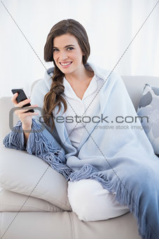 Pleased casual brown haired woman in white pajamas holding a mobile phone