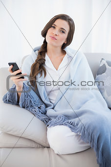 Attractive casual brown haired woman in white pajamas holding a mobile phone