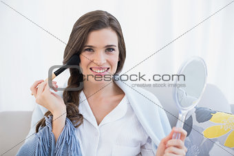 Delighted casual brown haired woman in white pajamas applying powder on her face