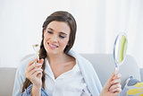 Pensive casual brown haired woman in white pajamas looking at her eyelash curler