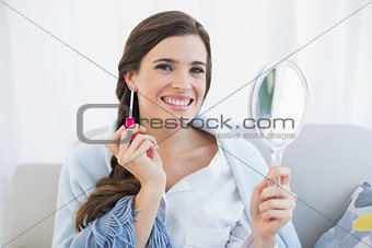 Happy casual brown haired woman in white pajamas applying gloss