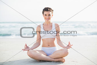 Smiling slim brown haired model in white sportswear meditating in lotus position