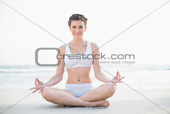Cheerful slim brown haired model in white sportswear meditating in lotus position