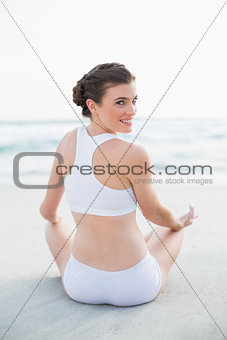 Happy slim brown haired model in white sportswear meditating in lotus position