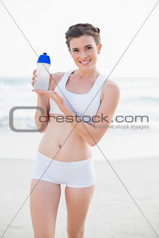 Pleased slim brown haired model in white sportswear showing her bottle of water