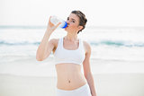Serious slim brown haired model in white sportswear drinking water
