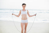 Smiling slim brown haired model in white sportswear playing with a skipping rope