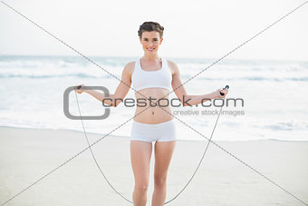 Smiling slim brown haired model in white sportswear playing with a skipping rope