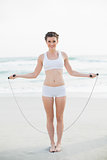 Content slim brown haired model in white sportswear playing with a skipping rope