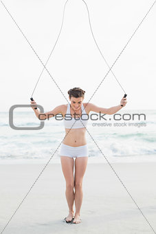 Dynamic slim brown haired model in white sportswear playing with a skipping rope