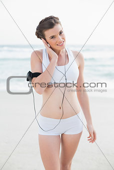 Pleased slim brown haired model in white sportswear listening to music
