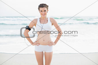 Cheerful slim brown haired model in white sportswear listening to music