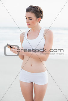 Charming slim brown haired model in white sportswear using her mobile phone