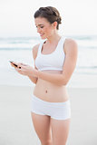 Cute slim brown haired model in white sportswear texting with her mobile phone