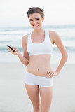 Content slim brown haired model in white sportswear holding a mobile phone