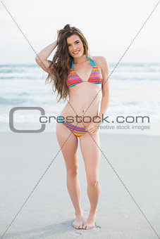 Pleased slim brown haired model in coloured bikini posing holding her hair