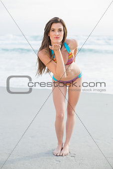 Seductive slim brown haired model in coloured bikini blowing a kiss to the camera