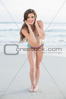 Cheerful slim brown haired model in coloured bikini posing holding her hair