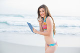 Charming slim brown haired model in coloured bikini holding a tablet pc