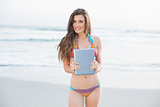 Cute slim brown haired model in coloured bikini holding a tablet pc