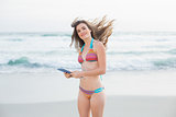 Joyful slim brown haired model in coloured bikini holding a tablet pc