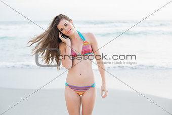 Thoughtful slim brown haired model in coloured bikini calling with her mobile phone