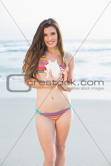 Happy slim brown haired model in coloured bikini holding a shell