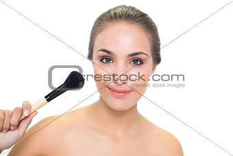 Smiling young brunette woman pointing a powder brush to her face