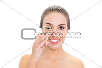 Smiling young brunette woman using an eyelash curler