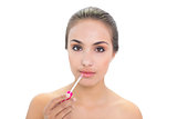 Content young brunette woman applying lip gloss