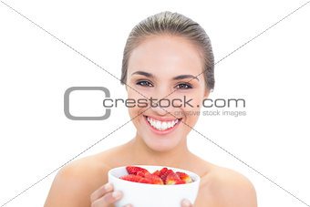 Cheerful young brunette woman holding a bowl of strawberries
